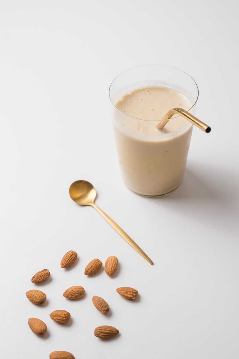 A minimalist shot of an almond milkshake with golden accents on a white background.